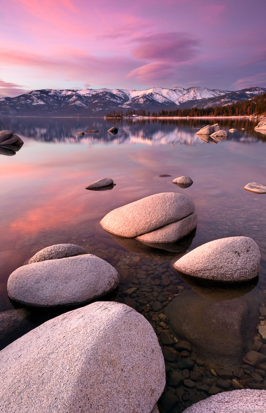 A pink sunset&nbsp;over the clear waters and boulders of Sand Harbor in Lake Tahoe.