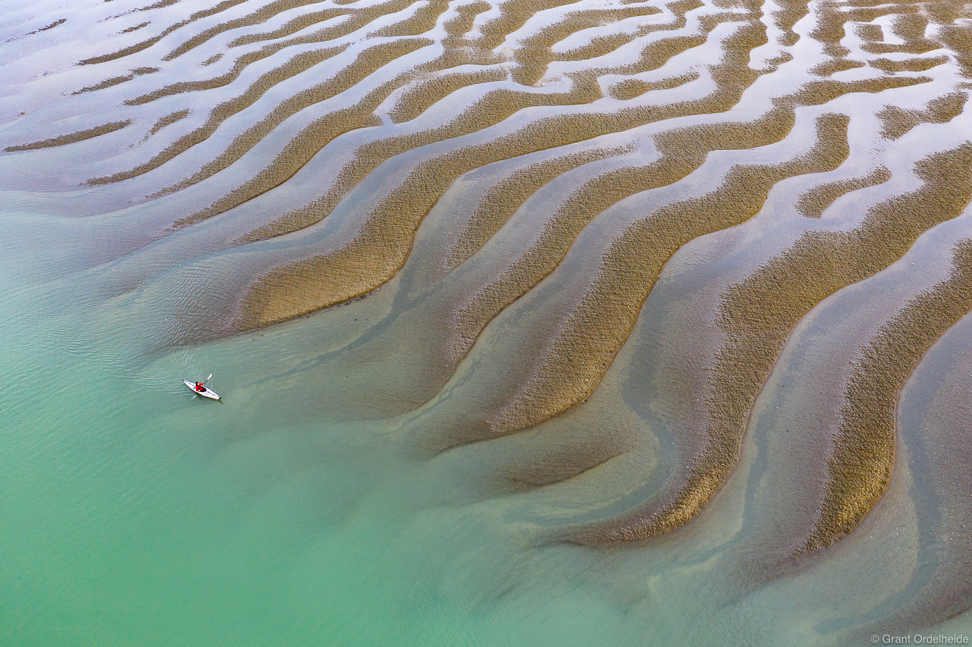 A kayaker paddling along sand textures at low tide off the shores of Mitkof Island in Southeast Alaska.