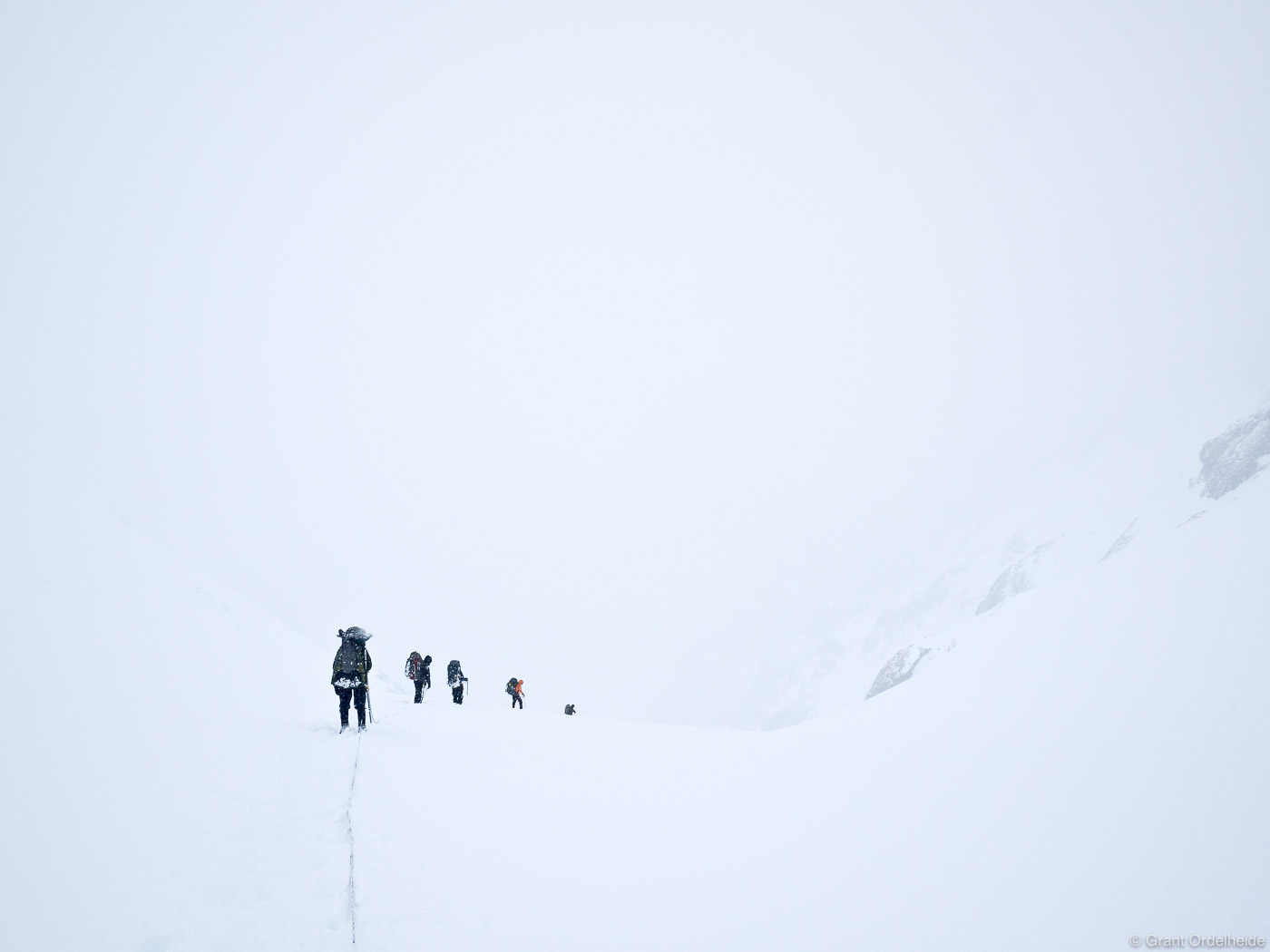 A rope teams decends a high pass during a whiteout storm.