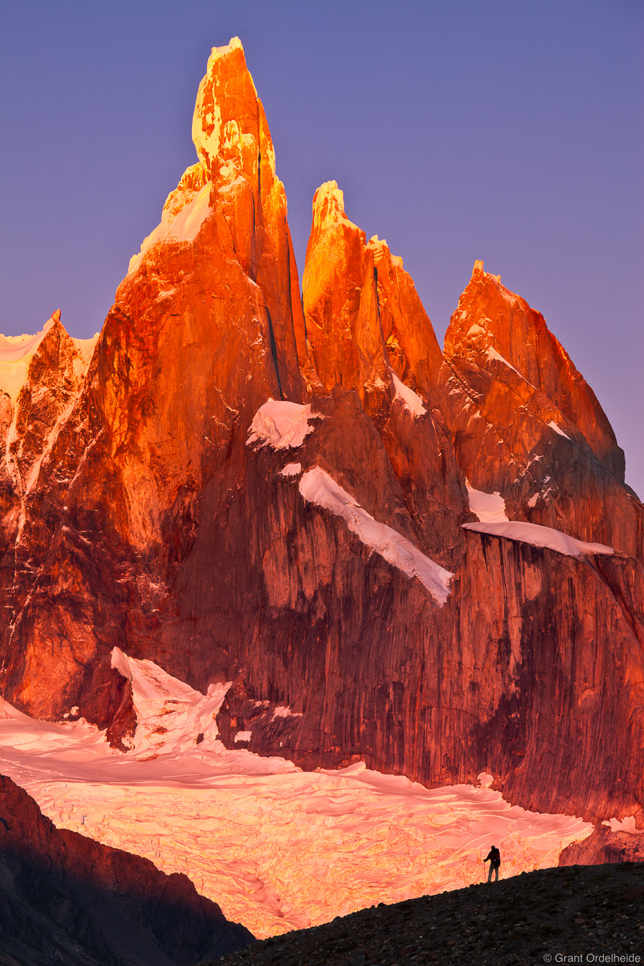 A hiker watches sunrise on the massive peaks of Cerro Torre, Cerro Egger, and Cerro Standhardt.