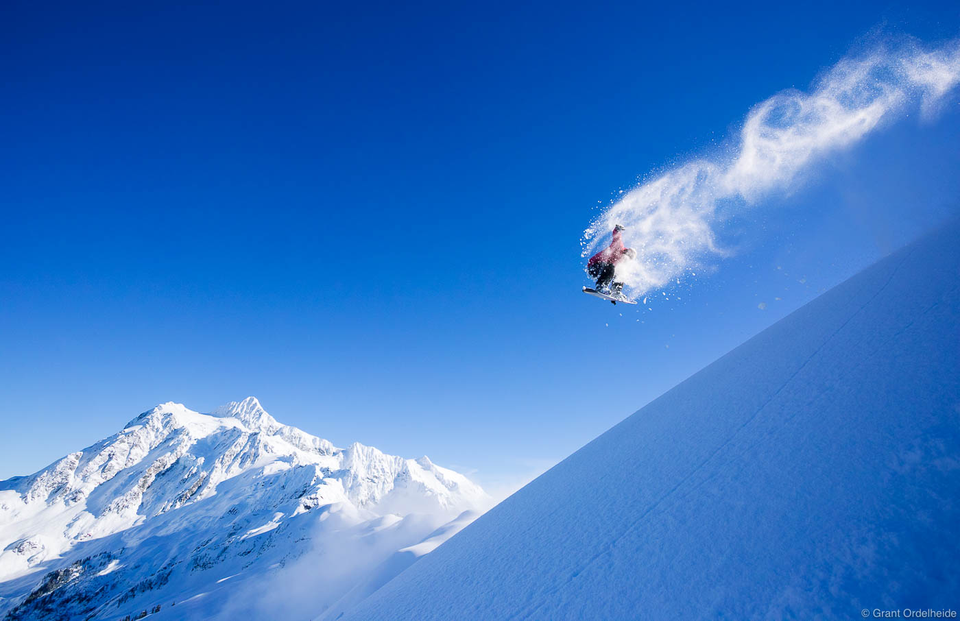 A snowboarder does a backside one-eighty method grab off of a natural wind lip feature.