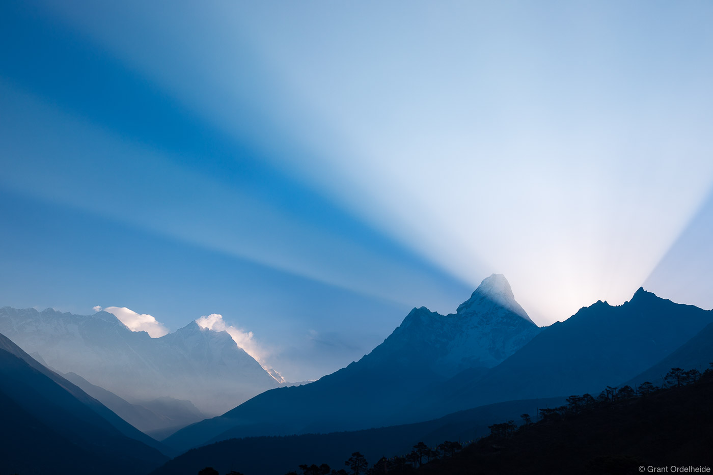 Light beams shoot up from behind Ama Dablam with Everest and Lhotse in the background viewed from the village of Tengboche.