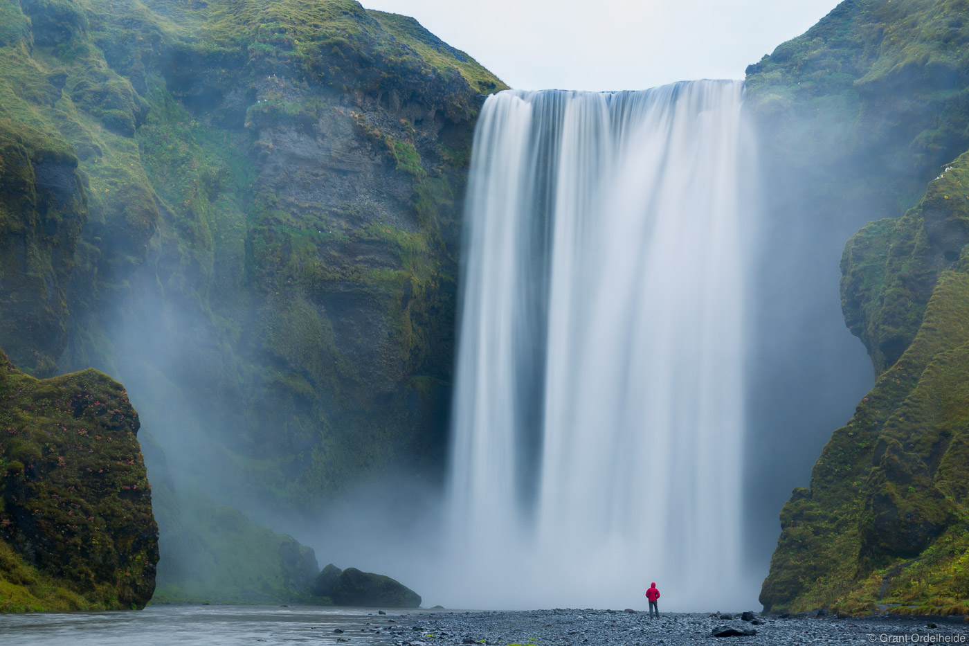 A person stands in front of the mighty Skógafoss, one of Iceland's biggest waterfalls.