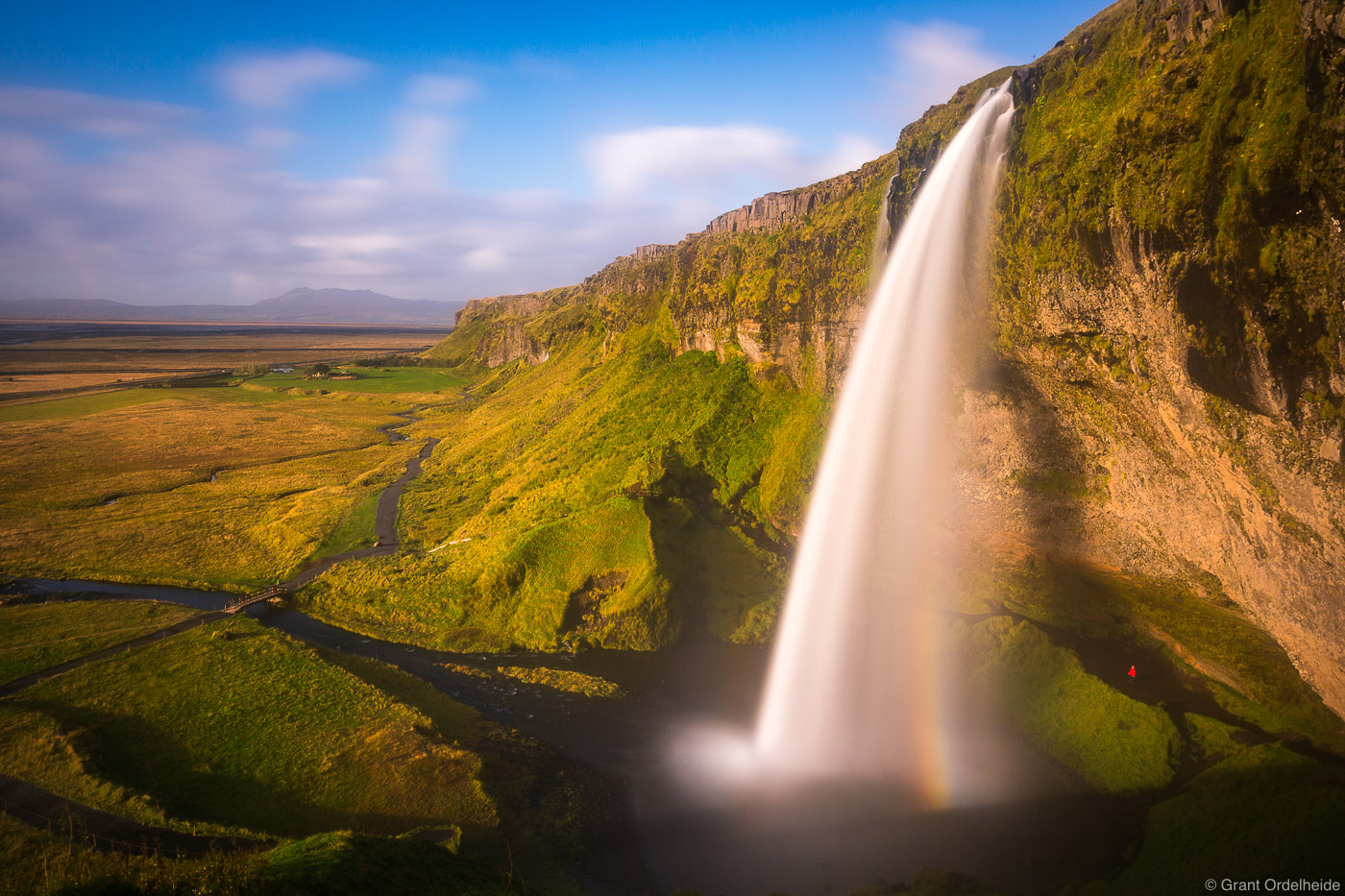 A person stands behind Seljandsfoss in Iceland at sunset.
