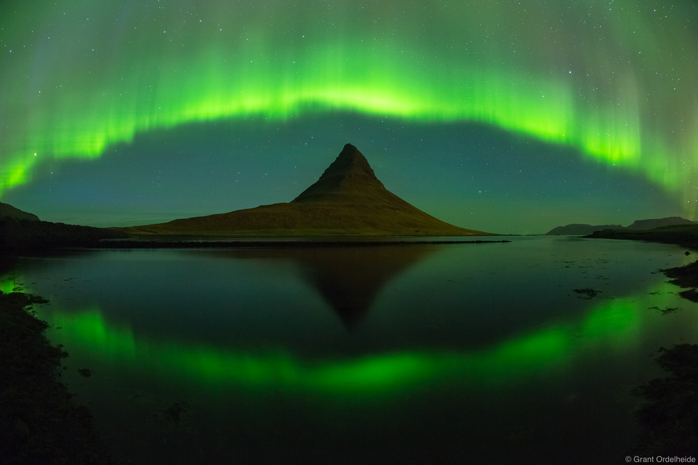 The Aurora Borealis arches over Kirkjufell mountain near Grundarfjörður, Iceland.