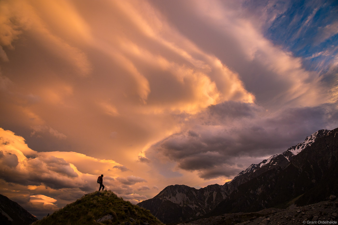 A hiker below a dramatic sunset along the Hooker Valley Track near Mt. Cook on New Zealand's South Island.