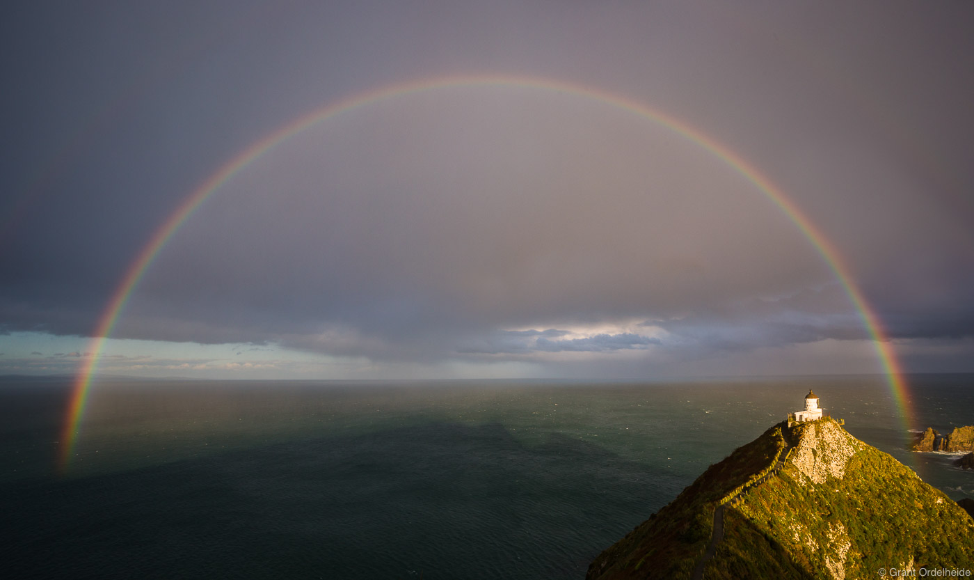 A rainbow over the Nugget Point Lighthouse along the coast of New Zealand's South Island.
