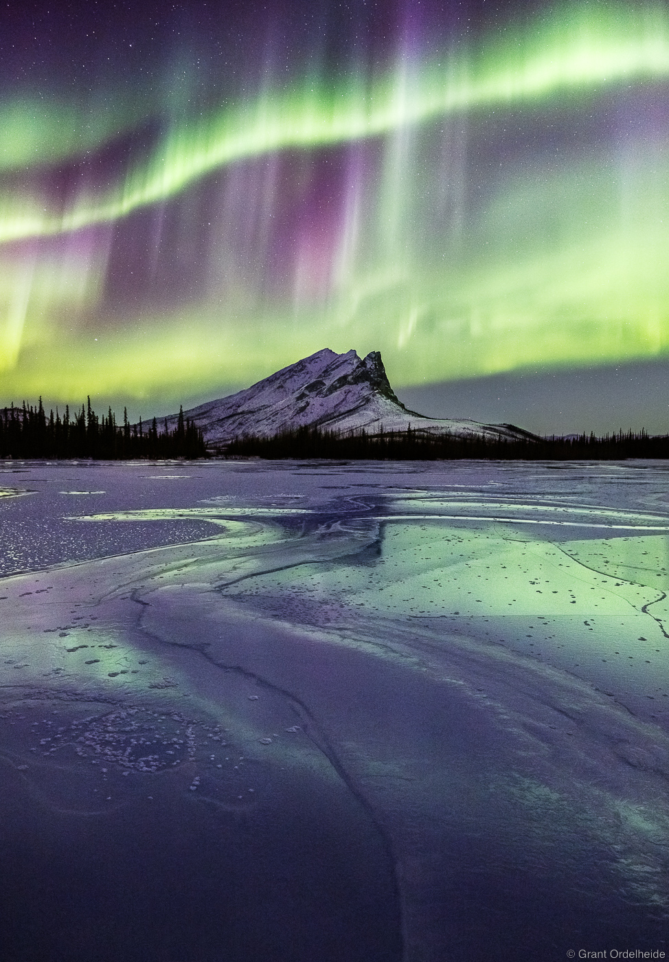 Northern lights over a frozen river and Sukakpak Mountain high above the Arctic Circle in Alaska.